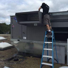 Northbrook, IL based Northfield Heating & Air employee standing on a ladder while working on a large HVAC unit